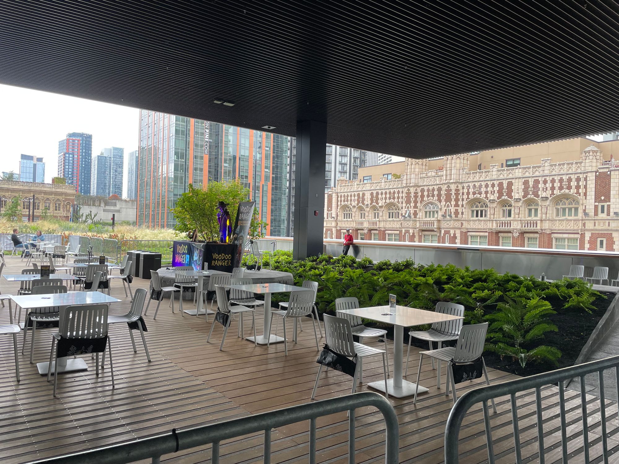 A covered patio atop a building in a city, with seats, a booth, and plants.