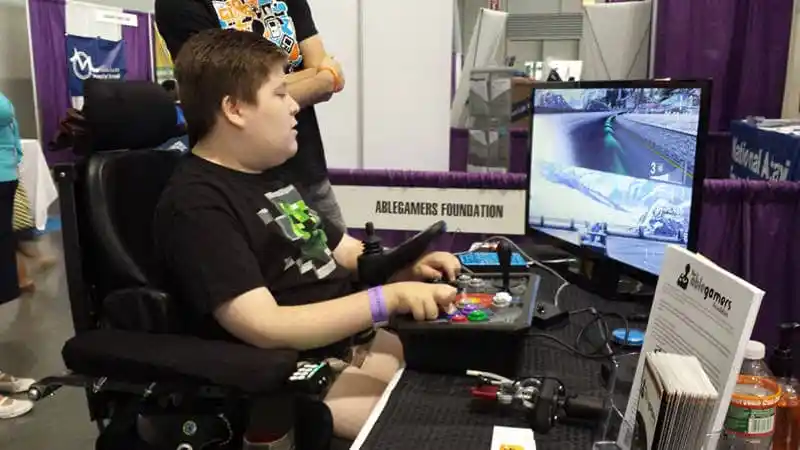 A photo of a young man in a power chair playing a racing game using an assistive controller. Image via AbleGamer's official site.
