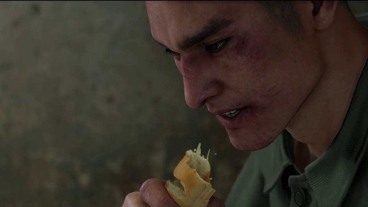 A bruised man violently taking a bite out of a fluffy piece of bread - a screenshot from Yakuza: Like a Dragon